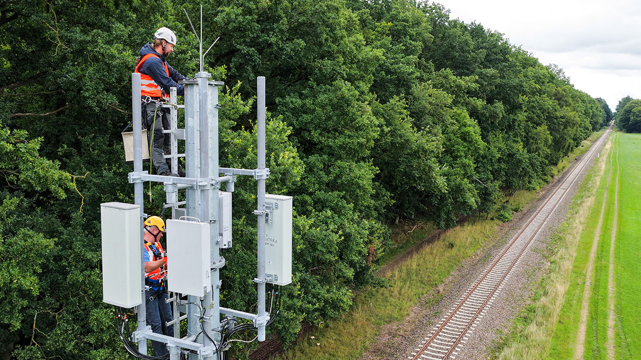 Zwei Netztechniker arbeiten an einer Mobilfunk-Antenne entlang einer Bahntrasse