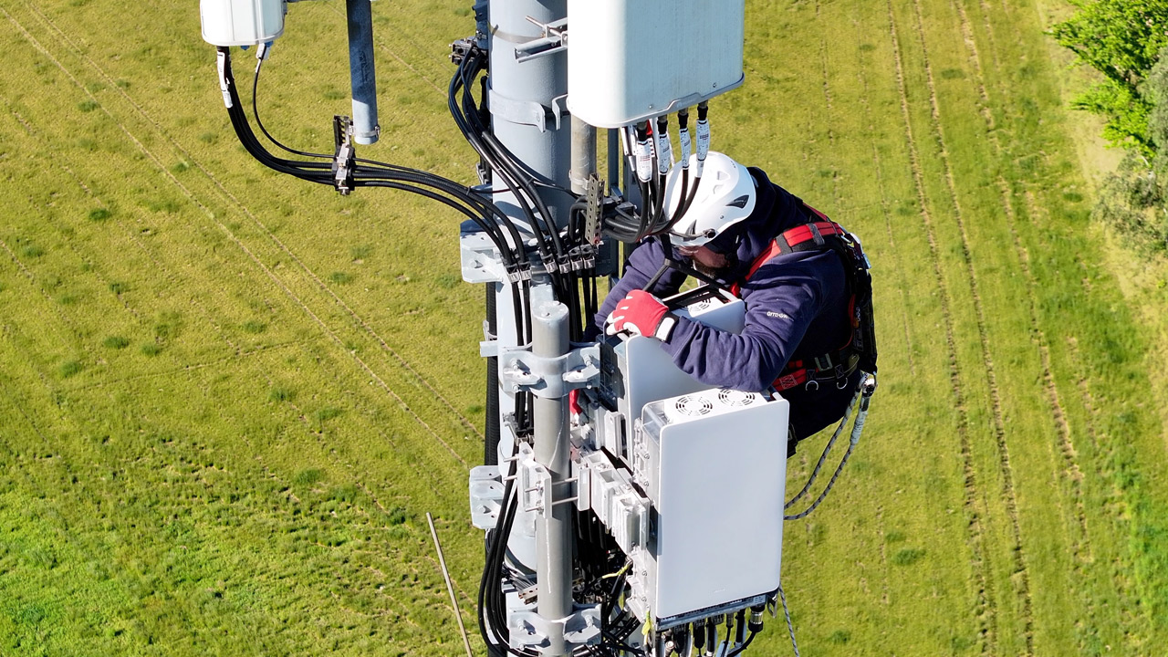 Luftaufnahme eines Technikers auf einem Mobilfunkmast in ländlichem Gebiet