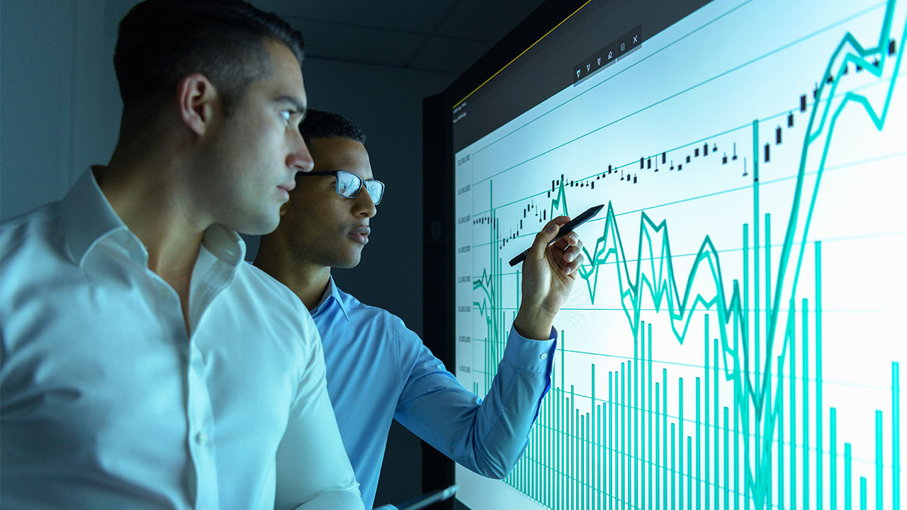 Zwei Geschäftsleute schauen Diagramme auf einem interaktiven Bildschirm an.